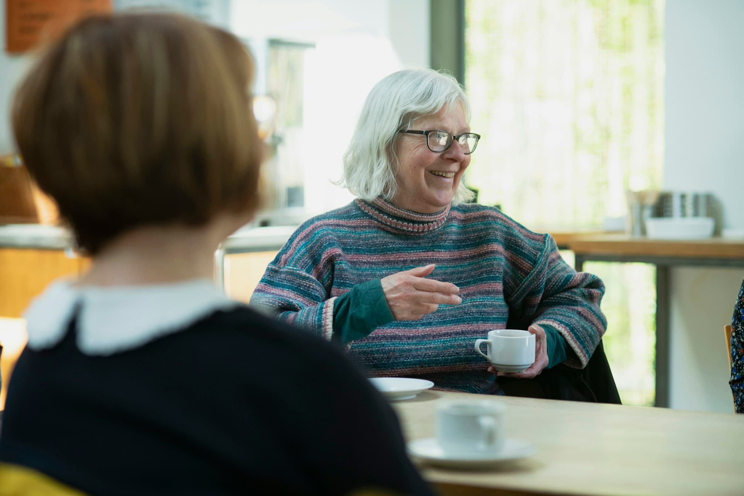 Two women talking over coffee at a table, one of them laughing
