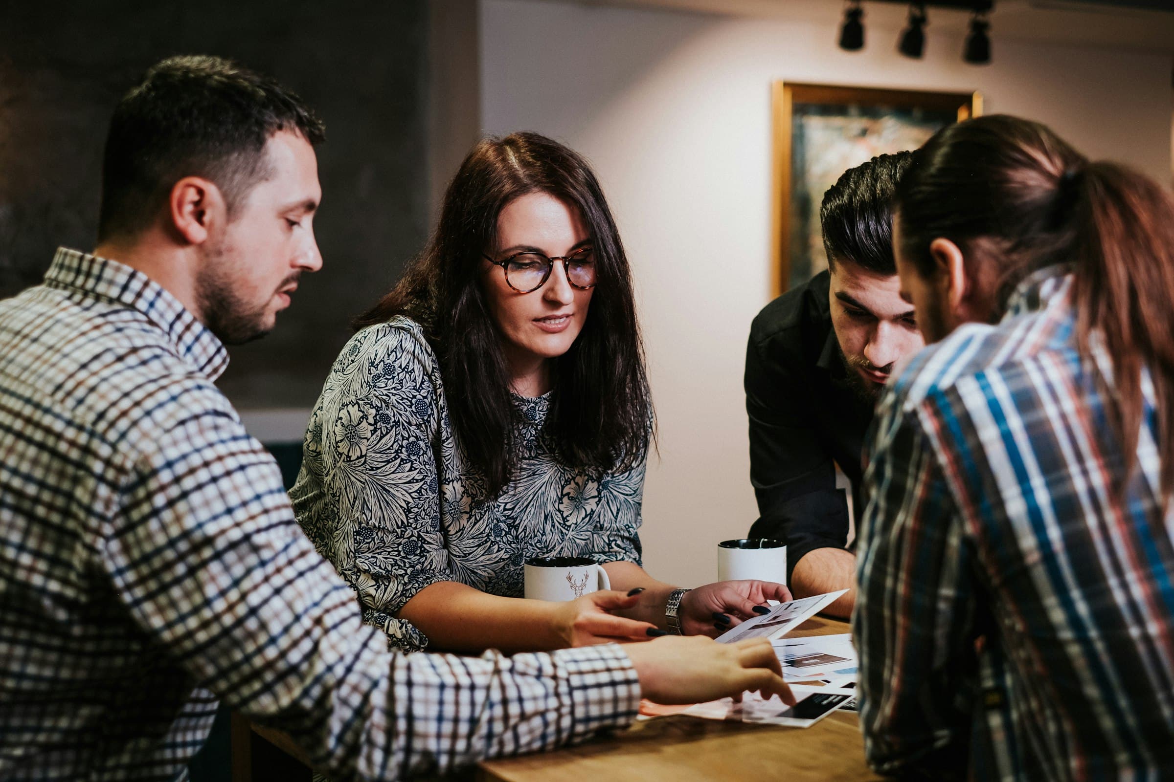 Four colleagues leaning over papers on a table, working through them together