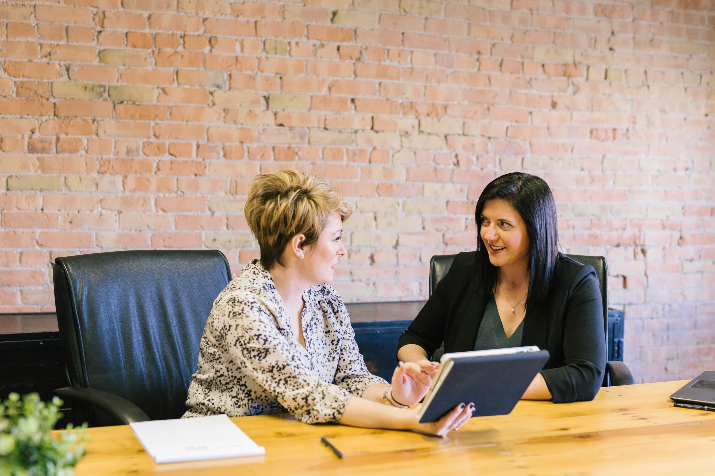 Two women at a boardroom table, going over a tablet together
