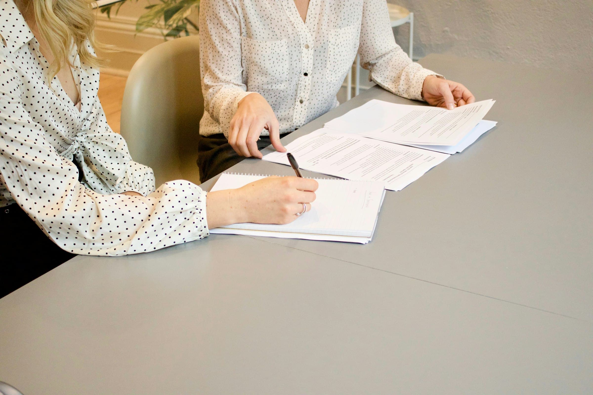 Two people at a table going through a printed document, one taking notes